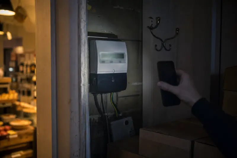 A hand shining a phone torch at an electricity meter in the back hallway of a small shop