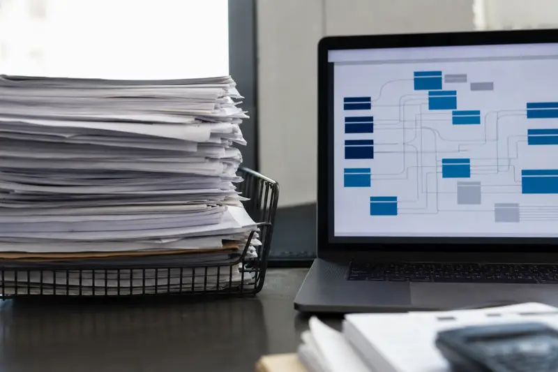 A tray of paper invoices next to a laptop showing structured data