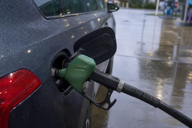 A fuel nozzle in a car's filler at a petrol station on a wet day
