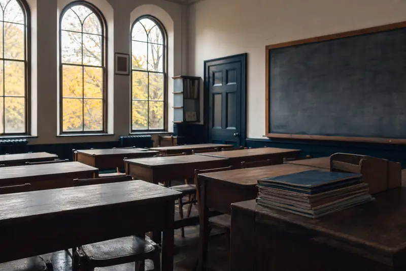 An empty classroom with wooden desks and tall arched windows
